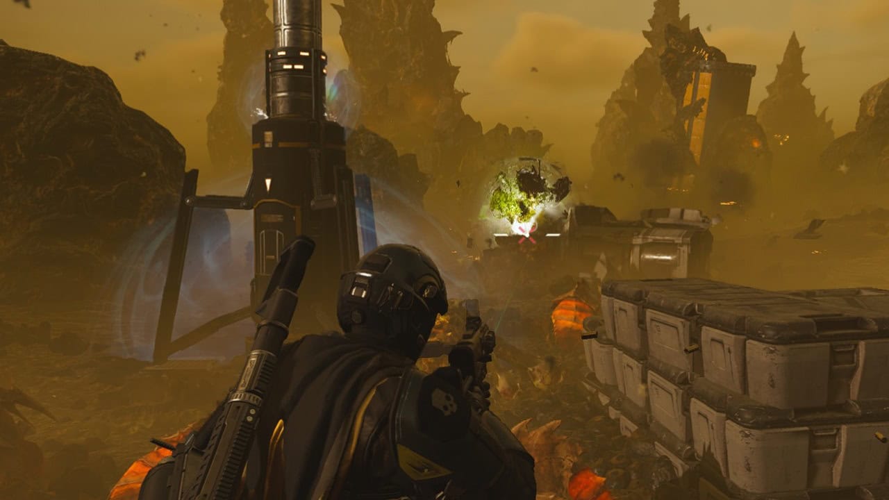 A Helldivers 2 soldier in futuristic armor crouches in a dusty, alien landscape with tall structures and scattered debris. Explosions and bright lights flare in the background, casting an eerie glow over the chaotic scene.