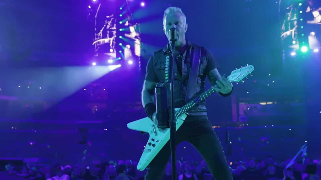 Un musicien se produit sur scène avec une guitare sous des lumières bleues et violettes, entouré d'une foule et de grands écrans en arrière-plan, créant l'atmosphère immersive de l'art clé de la saison 3 de Fortnite.